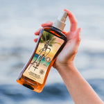 Hand holding a bottle of Panama Jack sunscreen oil with a blurred beach background