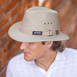 Man wearing a beige Panama Jack canvas safari hat against a brick wall.