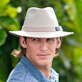 Man wearing a beige Panama Jack hat against a green blurred background