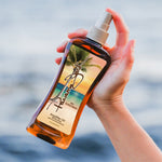 Hand holding a bottle of Panama Jack Amplifier Oil with a scenic label against a blurred water background