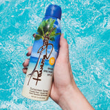 Hand holding a Panama Jack sunscreen spray can with a blue background