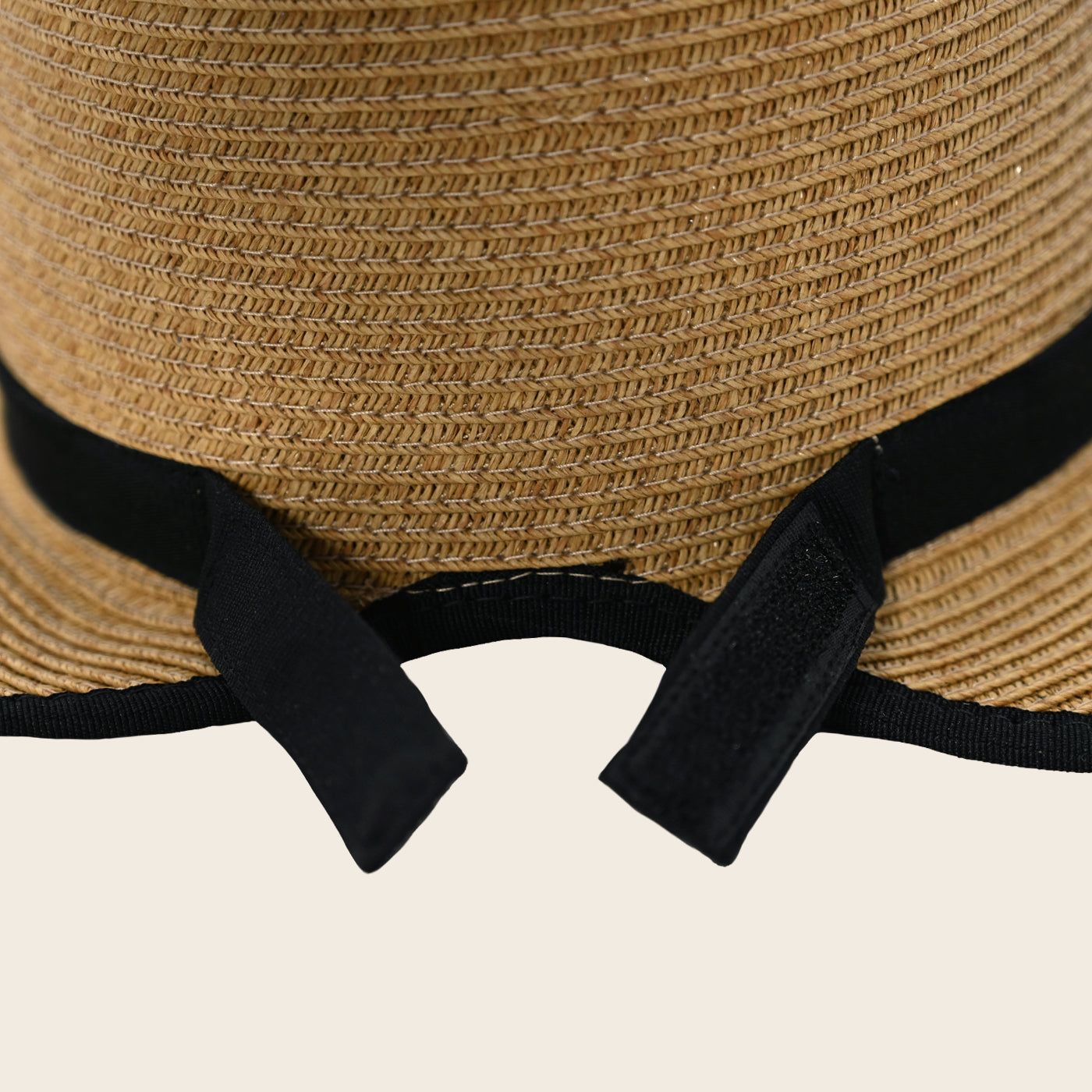 Close-up of a straw Panama Jack hat with black ribbon on a beige background