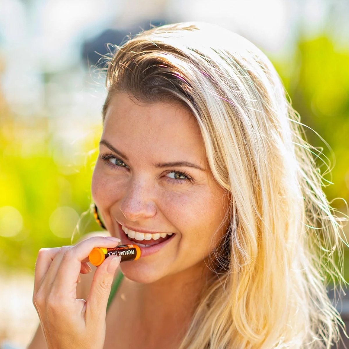 Woman holding an Panama Jack lip balm with a blurred outdoor background